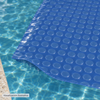 Visualización ilustrativa. Acercamiento de una sección de la cubierta solar azul CSK-2.5X1-BAP-4 sobre el agua, con la cara lisa hacia arriba y las burbujas hacia abajo. Se muestra un detalle de aplicación, no la cobertura completa de una piscina.